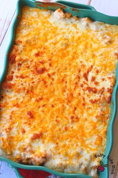 a green casserole dish filled with cheese on top of a white wooden table