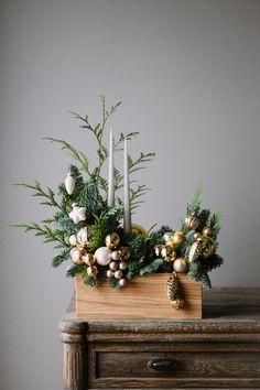 a wooden table topped with a vase filled with greenery and christmas decorations next to a lit candle