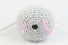 a gray crocheted ball with pink thread on the end and black hole in the middle