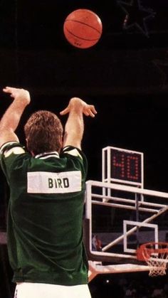 a man in green and white uniform shooting a basketball at a hoop with his hands