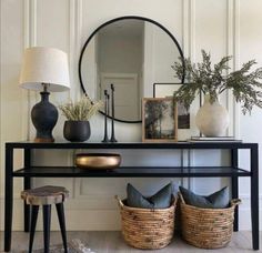 a black console table with two lamps and pictures on it, next to a round mirror