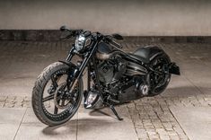 a black motorcycle parked on top of a cement floor next to a wall and sidewalk