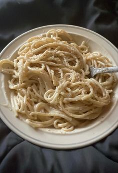 a white plate filled with pasta on top of a black cloth covered table next to a fork