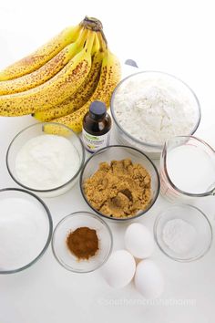 bananas, flour, eggs and other ingredients are arranged on a white counter top in bowls