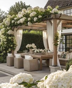 an outdoor dining area with white flowers and greenery on the arbor, surrounded by wicker furniture