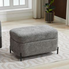 a grey ottoman sitting on top of a rug in a living room next to a window