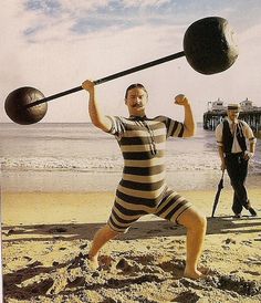 a man in striped shirt holding two large balls on top of his head while standing on beach