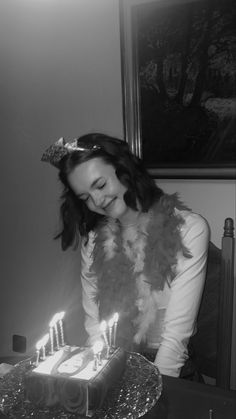 a woman sitting in front of a cake with lit candles on it and wearing a feather vest