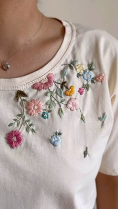 a woman wearing a white t - shirt with flowers embroidered on the chest and neck