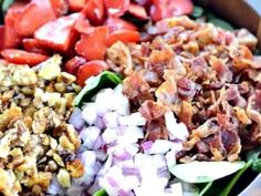 a close up of a salad in a box with tomatoes, onions and pecans