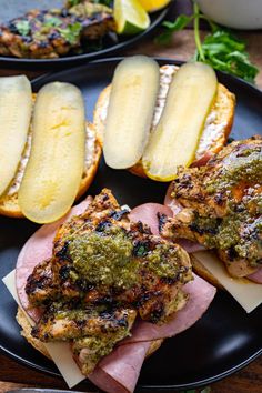 two black plates topped with sandwiches covered in pesto and cheese next to sliced pears