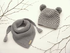 two knitted hats and scarfs sitting on top of a white table next to branches