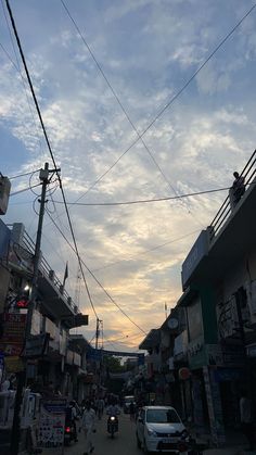 people are walking down the street in front of some buildings and power lines at sunset