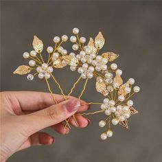 a hand holding a gold and white hair comb with pearls on it's head