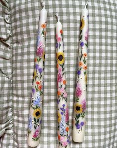 three candles with flowers painted on them are sitting on a checkered tablecloth surface