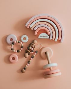 various beads and rings are laid out on a pink surface with a rainbow shaped object in the middle