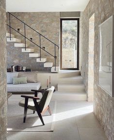 a living room filled with furniture next to a stone wall and stairs that lead up to the second floor