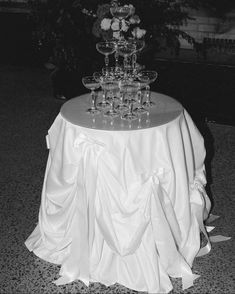 a table topped with lots of glasses on top of a white cloth covered round table