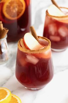 two glasses filled with red liquid and cinnamon stick garnished with an orange slice