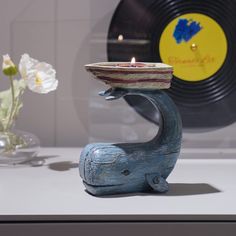 a blue elephant holding a bowl on it's back with a record in the background