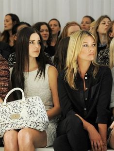 two women sitting next to each other in front of a crowd at a fashion show