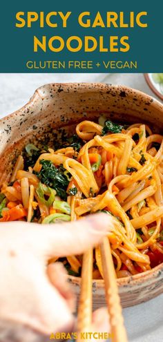 a person holding chopsticks over a bowl of noodles with spinach and carrots