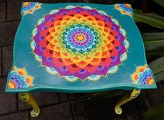 a colorfully painted bench sitting on top of a brick floor next to green plants