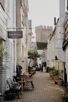 an alley way with chairs and potted plants on the side walk in front of buildings