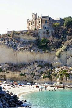 people are on the beach and in the water near an old castle perched on top of a cliff