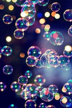 soap bubbles are floating in the air on a black background with multicolored lights