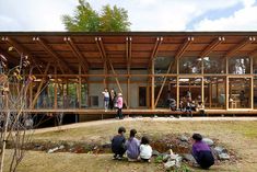 several people sitting on the ground in front of a building that is made out of wood