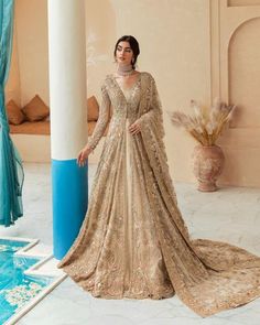 a woman standing in front of a pool wearing a gold and white gown with long sleeves