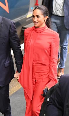 a woman in a red dress is holding hands with a man in a black suit