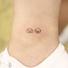 a small tattoo on the ankle of a woman's foot with two dogs sitting next to each other