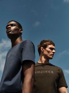 two men standing next to each other in front of a blue sky with white clouds