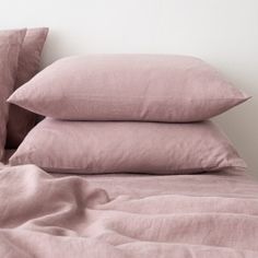 three pillows stacked on top of each other in front of a bed with pink sheets