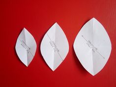 three pieces of paper that have been folded in the shape of leaves on a red surface