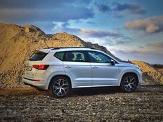 a white car is parked in front of some rocks and gravel with mountains behind it