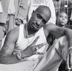 a black and white photo of a man with tattoos on his arm sitting in front of other men