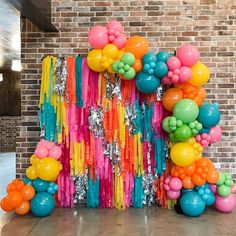 colorful balloons and streamers are on display in front of a brick wall