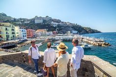 four people standing on the edge of a stone wall looking at boats in the water