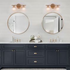 two round mirrors are above the double sinks in this blue bathroom with white shiping