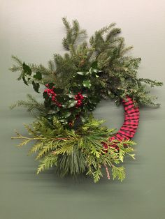 a christmas wreath hanging on the wall with evergreens and red plaid ribbon around it