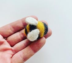 a hand is holding a small needle - felt bee