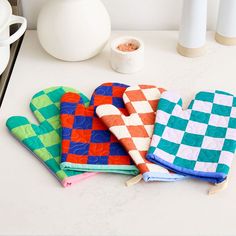 three oven mitts are sitting on a counter next to a vase and other kitchen accessories