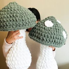 two crocheted hats are being held up to the side by someone's hands