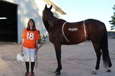 a woman in an orange shirt standing next to a brown horse with a football painted on it's face