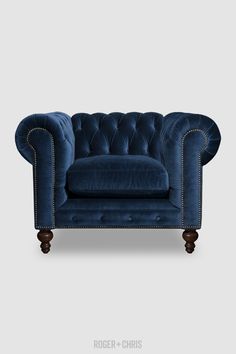 a blue velvet couch with wooden legs and buttons on the back, in front of a gray background