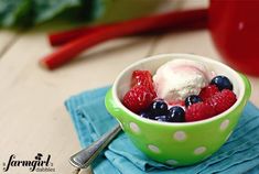 a green bowl filled with berries and ice cream on top of a blue napkin next to a red pepper shaker