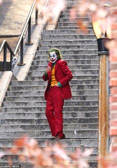 a man dressed as the joker walking down some stairs with his hand in his mouth